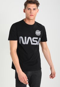 Camiseta negra de algodón con un destacado logo plateado de "NASA" en la parte frontal y un pequeño emblema circular de NASA en el lado izquierdo del pecho. Mangas cortas.