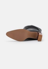 Bottine en cuir noir avec une surface texturée, dotée d'un talon bloc marron et d'une semelle lisse et arrondie.