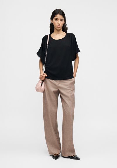 Μαύρο φαρδύ τοπ, μπεζ παντελόνι με φαρδιά μπατζάκια και μαύρα μυτερά φλατ παπούτσια. Αξεσουάρ είναι μια μικρή ροζ τσάντα με λουρί αλυσίδα.