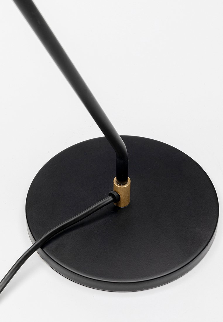 Lámpara de mesa de metal negro con base redonda, vástago delgado y conexión de hardware en latón. Presenta un cordón de alimentación negro adjunto.