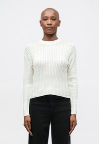 Suéter branco de malha com um padrão de cabo texturizado, decote redondo e punhos canelados, combinado com calças pretas justas.