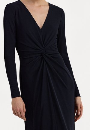 Langärmliges schwarzes Kleid mit V-Ausschnitt und gedrehtem Detail an der Taille. Aus glattem Stoff gefertigt und hat eine drapierte Textur im Rock.