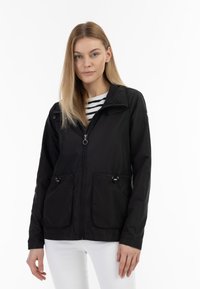 Giacca leggera nera con due tasche frontali, chiusura con zip, cordoncino regolabile e colletto. Abbinata a una maglia a righe bianco e nere.