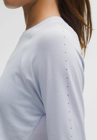 Világoskék sport hosszúujjú póló, amely texturált anyagból készült, perforált részletekkel a vállvarrat mentén, a légáteresztés érdekében.