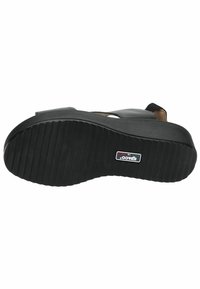 Sole nera di scarpa con una superficie in gomma testurizzata, caratterizzata da scanalature orizzontali per la trazione e un’etichetta con il logo che indica il marchio.