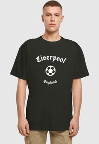 Zwarte katoenen t-shirt met witte "Liverpool" tekst, een grafische afbeelding van een voetbal en "England" eronder. Klassiek unisex ontwerp.