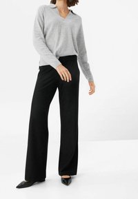 Ljusgrå långärmad tröja med v-ringning och krage; tillsammans med svarta vida byxor och spetsiga svarta lägenheter.