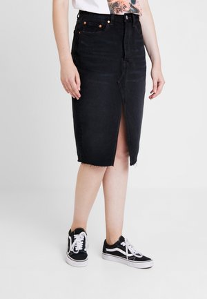 Woman wearing a black knee-length denim skirt with a front slit and raw hem, paired with black and white lace-up sneakers.