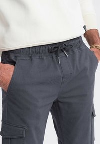 Grå cargo bukser med elastisk talje og snor. Har sidelommer og en afslappet pasform. Materialet virker holdbart med en glat tekstur.