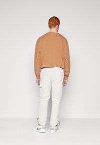 Brun crewneck sweatshirt, vita cargobyxor med sidofickor och vita sneakers med blå och svarta accenter. Avslappnad passform, lätt textur.