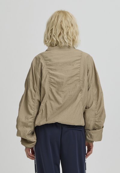 Veste beige texturée avec une coupe décontractée, manches froncées et col montant. Présente des coutures arrière et un design court.