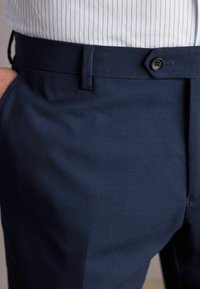 Marineblaues Modell mit strukturiertem Stoff, Knopfverschluss und Seitentaschen. Der Bund sitzt oberhalb der Hüften und hat eine taillierte Passform.