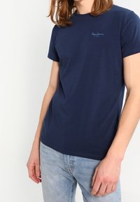 Granatowa krótkosleeva bawełniana koszulka z okrągłym dekoltem i małym detalem logo na piersi. Nosić z jasnoniebieskimi dżinsami.