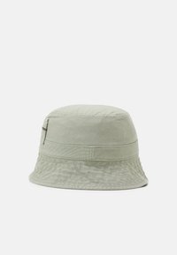 Gorra de cubo verde claro hecha de tejido texturizado. Presenta un ala ancha y una banda horizontal alrededor de la corona. Diseño simple con un acento sutil.