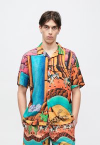 Πουκάμισο με κοντά μανίκια που διαθέτει πολύχρωμο, εμπριμέ σχέδιο με τοπία, ζώα και ζωηρές αποχρώσεις πορτοκαλί, μπλε, πράσινου και ροζ.