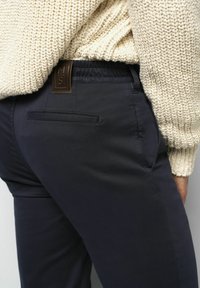 Pantalon navy à coupe slim, comportant une poche arrière, une ceinture élastique et un pull en tricot beige texturé partiellement visible.