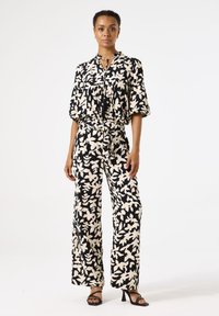 Zwart-witte jumpsuit met bloemenprint, korte mouwen, een trekkoord in de taille, wijde benen en een strikdetail op de halslijn.