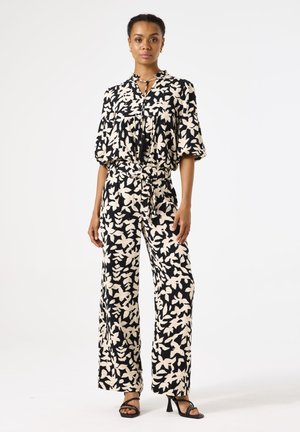 Zwart-witte jumpsuit met bloemenprint, korte mouwen, een trekkoord in de taille, wijde benen en een strikdetail op de halslijn.