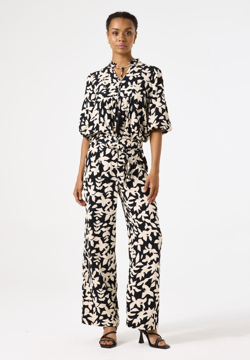 Zwart-witte jumpsuit met bloemenprint, korte mouwen, een trekkoord in de taille, wijde benen en een strikdetail op de halslijn.