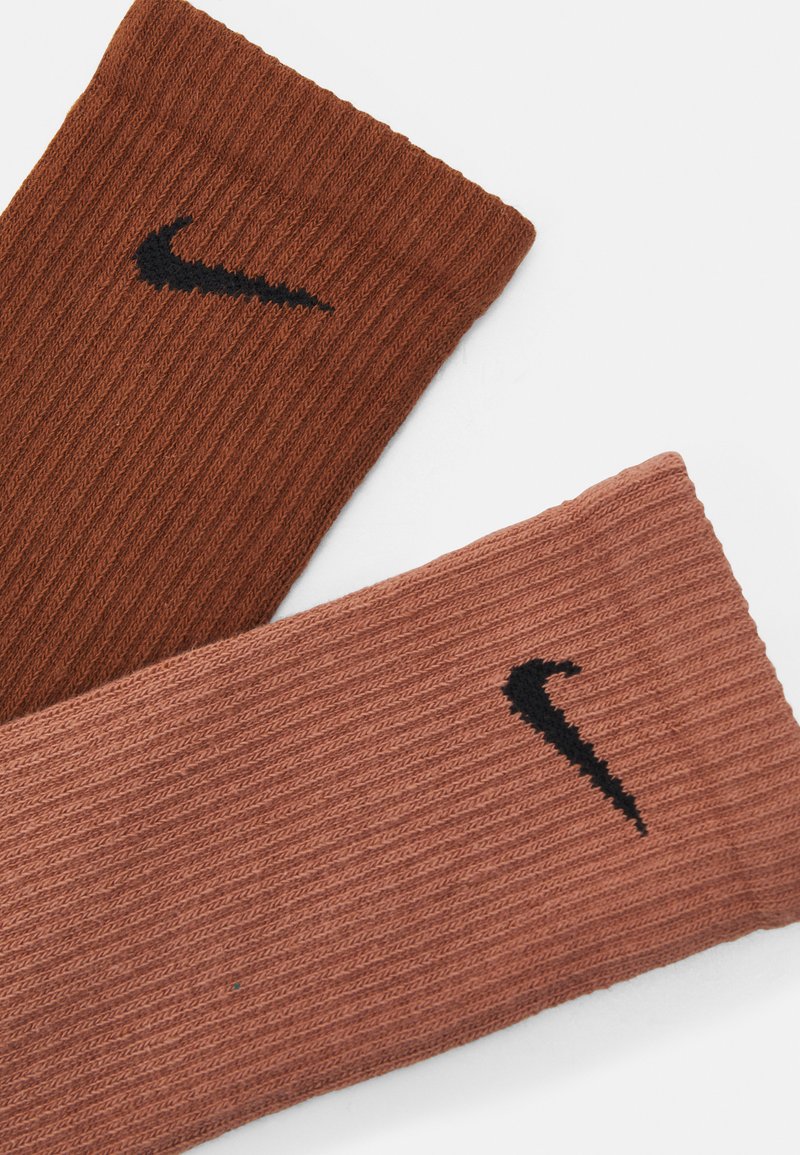 Dwie pary skarpet prążkowanych w ciemnym brązie i jasnym różu, z czarnym logo Nike na każdej skarpecie. Miękka faktura i casualowy design.