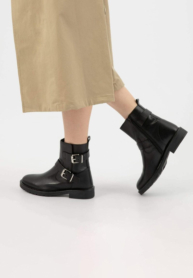 Czarne skórzane botki za kostkę z dwoma srebrnymi klamrami, okrągłym noskiem i niskim obcasem. Zamek błyskawiczny po boku, teksturowana gumowa podeszwa.