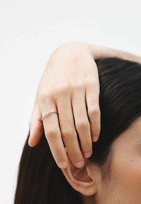 Anillo de plata con tres pequeñas piedras transparentes engastadas en una delicada banda, usado en una mano que toca un cabello oscuro y lacio junto a una oreja.