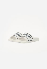 Sandale albe tip slide cu o bandă lată cu branding negru, talpă plată și textură netedă, concepute pentru confort și purtare casuală.