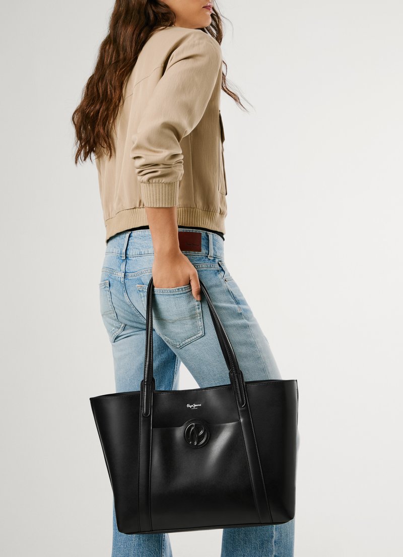 Saco de mão de couro preto com alças duplas, apresentando um bolso frontal e um emblema circular. Textura suave com design minimalista.