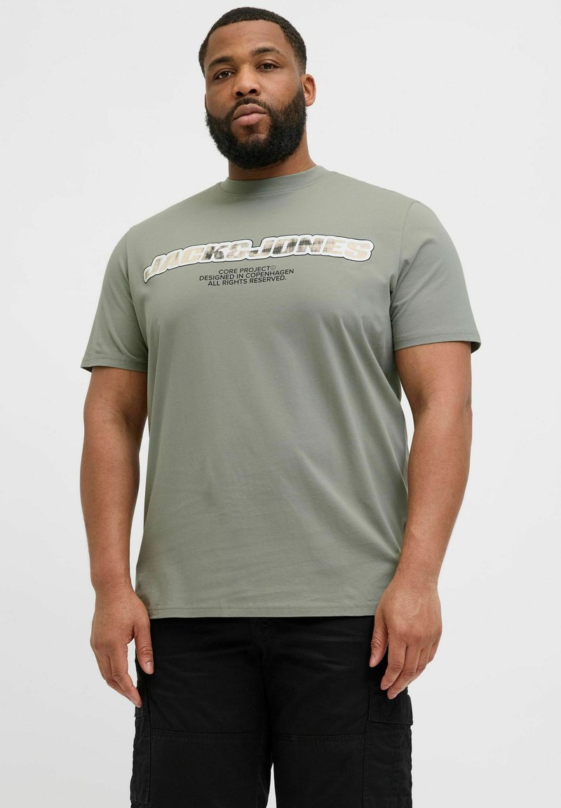 Oliven grøn t-shirt i bomuld med et stort grafisk tryk "JACK & JONES" tværs over forsiden i hvidt og gråt, rund halsudskæring, korte ærmer.