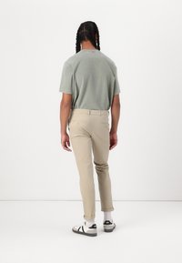 Lysegrøn kortærmet skjorte parret med beige slim-fit bukser, som har baglommer med guld hardware, og sort-hvide sneakers.