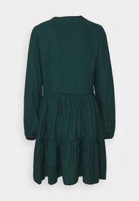 Robe longue à manches longues vert foncé avec une jupe à volants, présentant un col rond et une texture de tissu lisse. Aucun motif ou matériel visible.