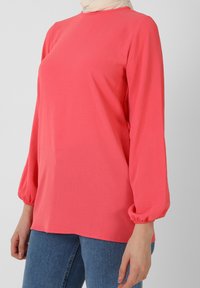 Maglietta coral a manica lunga con scollo rotondo e polsini elasticizzati, realizzata in tessuto leggero. Abbinata a jeans blu a vita alta.