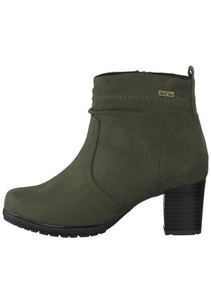 Zamszowy botek do kostki w kolorze oliwkowej zieleni z bocznym zamkiem błyskawicznym, grubym obcasem i oznaczoną metką przy mankiecie.
