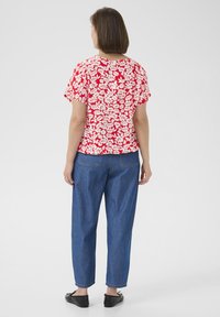 Haut à manches courtes à motifs floraux rouges associé à un pantalon en denim bleu ample et des chaussures noires à enfiler, vu de dos.