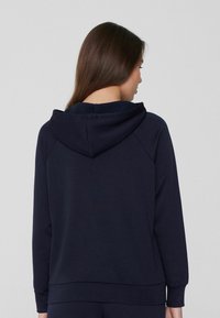 Sudadera con capucha azul marino hecha de una tela suave, que presenta mangas raglán, un bolsillo de canguro y puños y dobladillo acanalados.