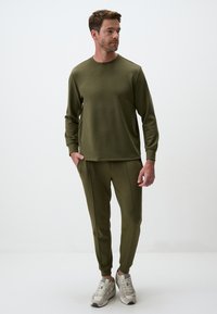 Olive green sweatshirt and matching joggers in soft fabric. Slim fit with ribbed cuffs and side pockets. Paired with light-colored sneakers.