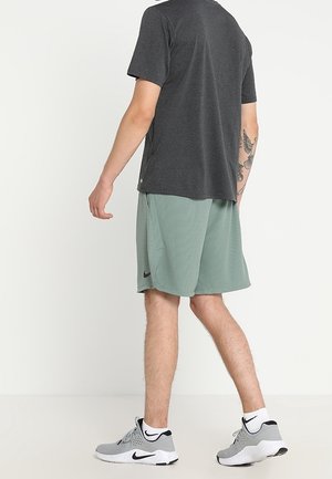 Tenue de sport pour homme comprenant un t-shirt gris foncé et un short vert clair, tous deux en tissu léger. Chaussures blanches avec des accents noirs.