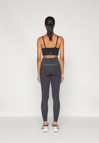 Brassiere sportivo nero, leggings aderenti grigi scuri, texture liscia, cuciture verticali, punto di contrasto, abbinati a scarpe da ginnastica bianche.
