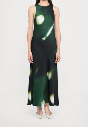 Robe longue sans manches avec un motif abstrait vert foncé et noir et des chaussures blanches pointues sur une femme debout.