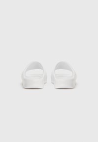 Des sandales blanches à enfiler avec une finition lisse et mate, un talon ouvert et des bords arrondis. Conçues avec une silhouette minimaliste et sans couture.