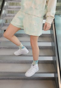 Mátové šňůrové šortky s bílým logem Nike, doplněné bílými vysokými teniskami a ponožkami s světle modro-zeleným gradientem.