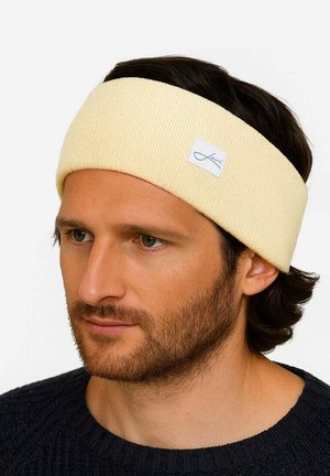 Gelbes, geripptes Stoffhaarband mit einem gestickten Logo-Tag, das über dunklem Haar getragen wird, mit einer glatten Textur und mittlerer Breite.