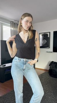Top nero avvolgente con maniche corte, abbinato a jeans a vita alta di colore blu chiaro. L'outfit è accessorato con orecchini a cerchio dorati.