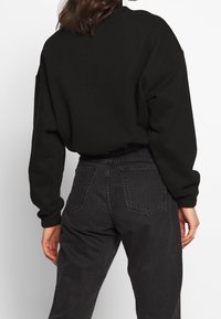 Black sweatshirt with a loose fit, ribbed cuffs, and waistband, paired with high-waisted, dark denim jeans featuring back pockets.