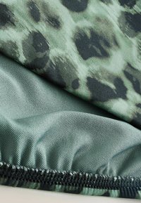 Tissu vert avec un motif léopard en noir et vert foncé. Texture lisse avec un détail de bas plissé.