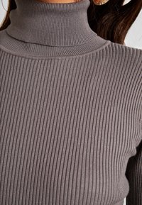 Gray ribbed turtleneck sweater with a close fit. Features vertical stripes, a high collar, and a soft texture.