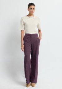 Haut crème à manches courtes avec un col orné, associé à un pantalon large violet taille haute et des talons taupe. Textures lisses, coupe cintrée.