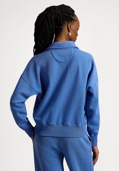 Μπλε φούτερ από απαλό ύφασμα με χαλαρή εφαρμογή, διαθέτει ψηλό λαιμό, πέφτοντες ώμους και ριμπ τελειώματα στα μανίκια και στο κάτω μέρος.