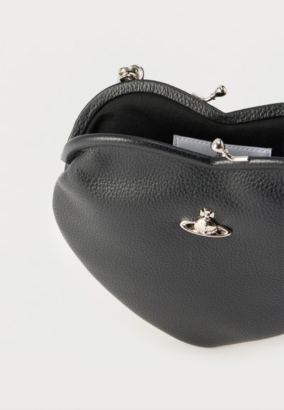 Μαύρο πορτοφόλι νομισμάτων από δέρμα με υφή, με ασημένιο κούμπωμα και μικρό ασημένιο έμβλημα σχήματος σφαίρας στο μπροστινό μέρος, εμφανιζόμενο μερικώς ανοιχτό σε λευκό φόντο.