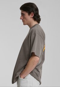 Camiseta gris de gran tamaño con mangas cortas, que presenta un escote redondo y un gráfico naranja en la parte posterior. Textura de algodón suave.
